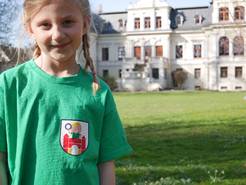 Ein Mädchen mit Kinderstadt-Shirt steht im Amtsgarten Ottersleben vor der Villa Böckelmann