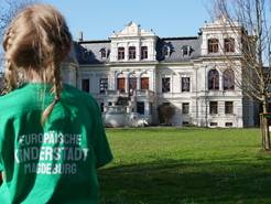 Ein Mädchen mit Kinderstadt-Shirt steht im Amtsgarten Ottersleben vor der Villa Böckelmann